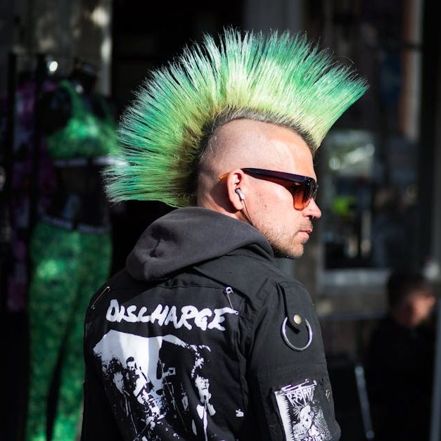Portrait of a punk fashion enthusiast in England with a striking green mohawk and sunglasses.
